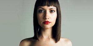 A woman model with straight, shoulder-length dark brown hair against a gray background.